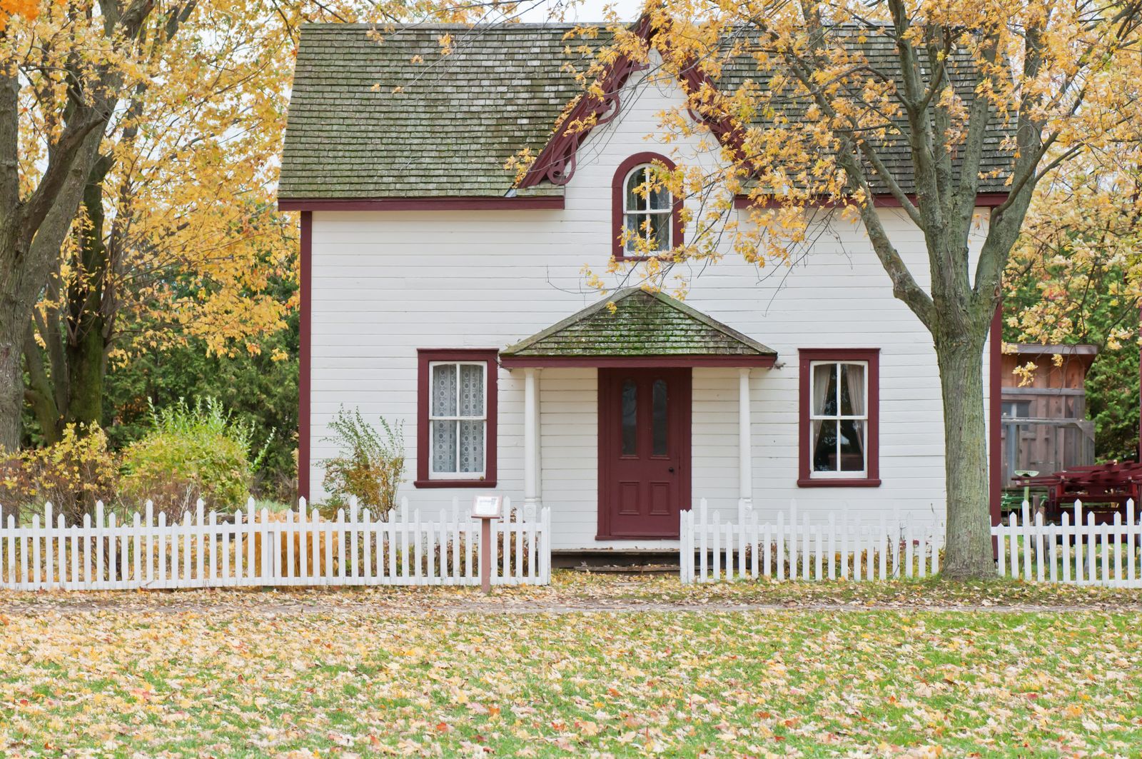 A white cottage with a picket fence surrounded by fall foliage