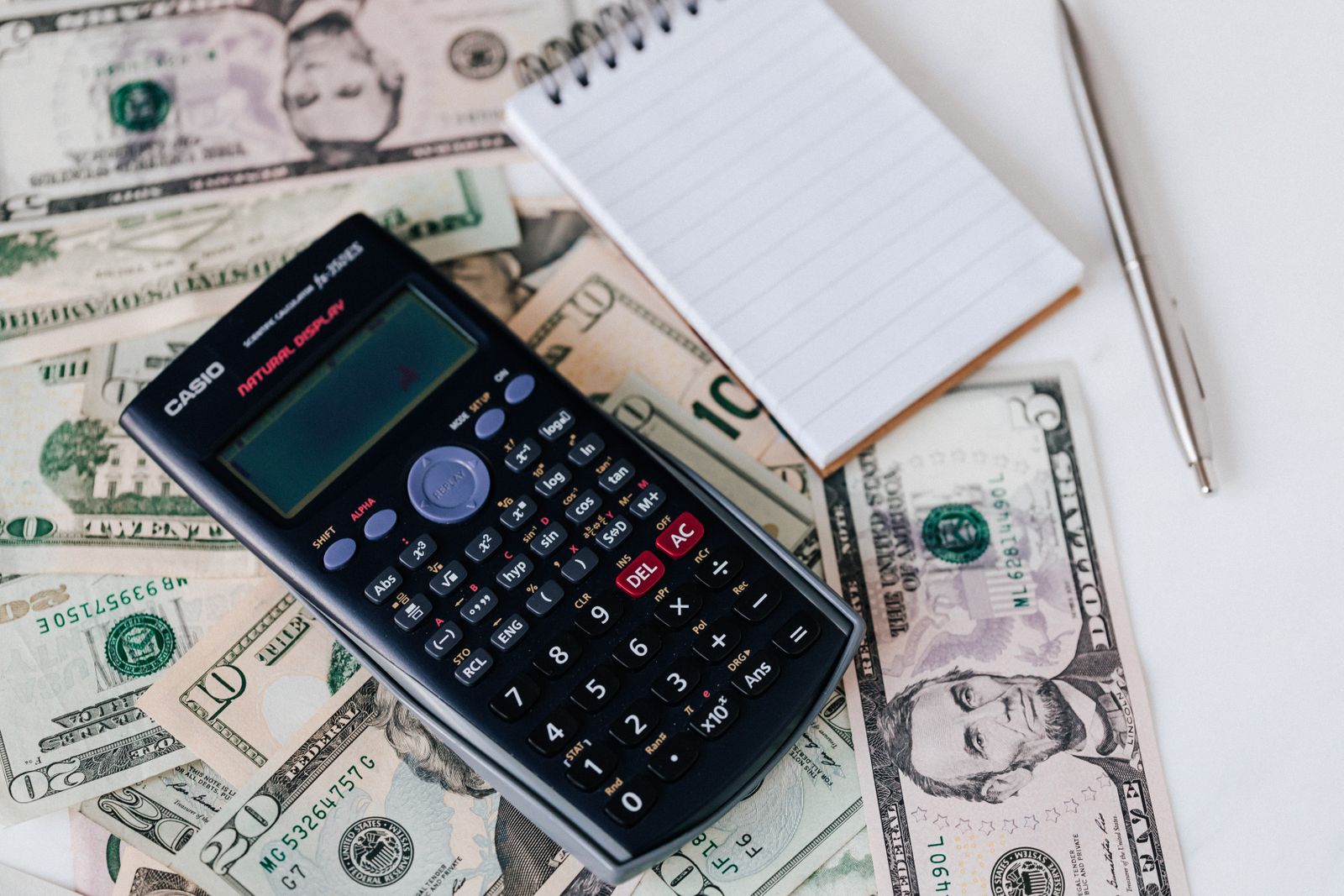 A calculator and notepad resting on a spread of dollar bills